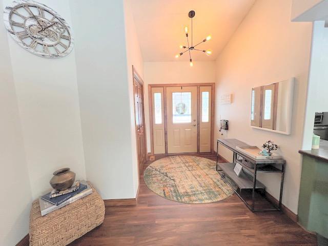 foyer with high vaulted ceiling, an inviting chandelier, and dark wood-type flooring