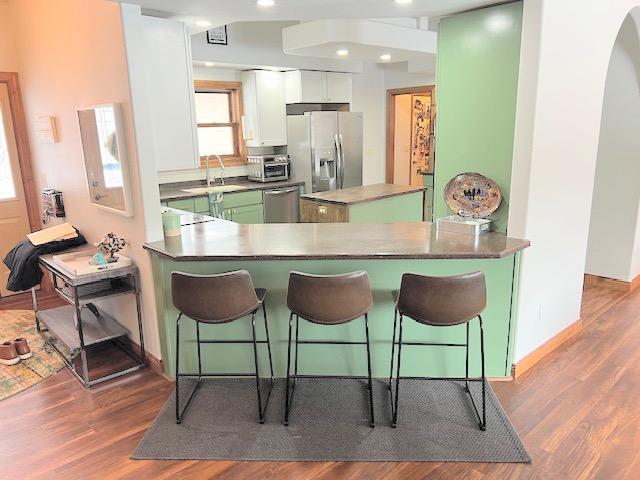 kitchen with a kitchen breakfast bar, kitchen peninsula, white cabinetry, and appliances with stainless steel finishes