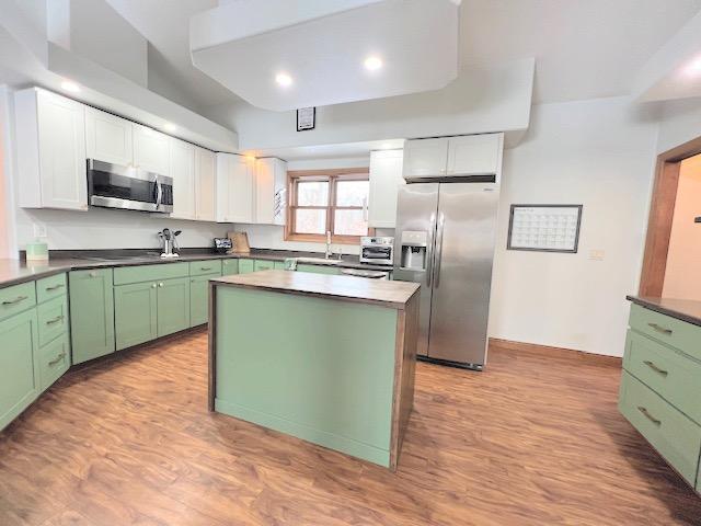 kitchen with white cabinetry, green cabinets, light hardwood / wood-style floors, a kitchen island, and appliances with stainless steel finishes