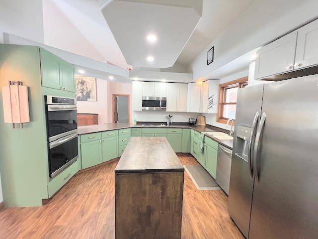 kitchen featuring kitchen peninsula, white cabinets, stainless steel appliances, and light wood-type flooring