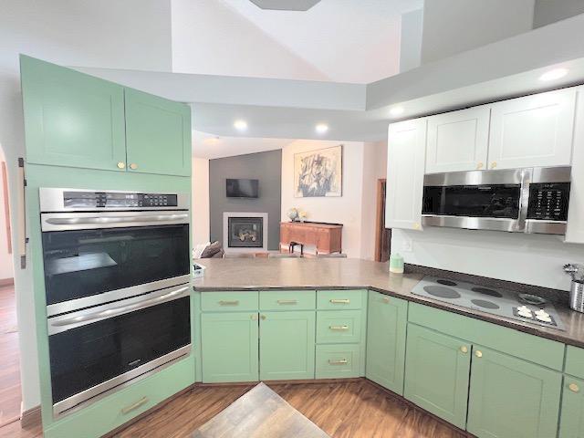 kitchen with green cabinetry, kitchen peninsula, appliances with stainless steel finishes, and light hardwood / wood-style flooring