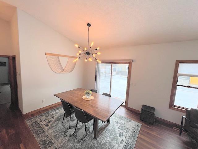 dining space featuring dark hardwood / wood-style floors, lofted ceiling, and a chandelier