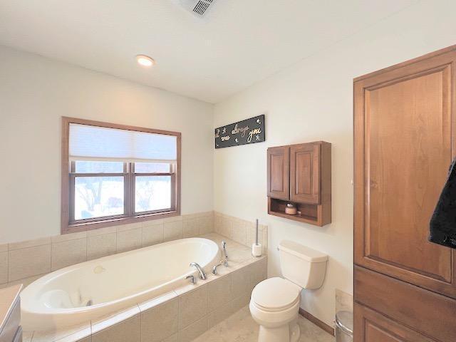 bathroom featuring vanity, tiled bath, and toilet