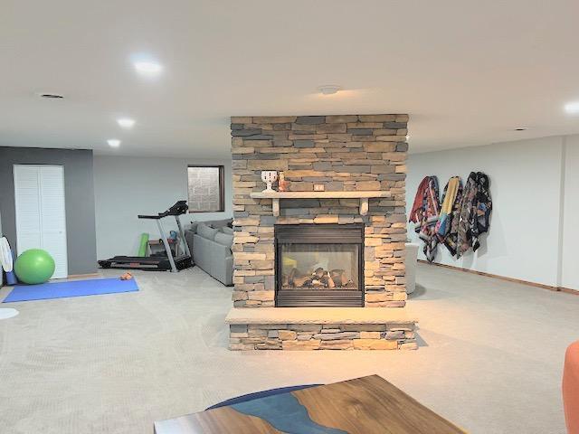 carpeted living room featuring a stone fireplace