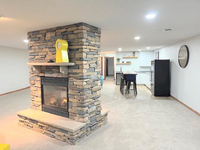 unfurnished living room featuring a stone fireplace and light colored carpet