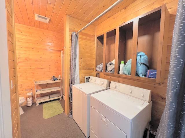 clothes washing area featuring washer and dryer, dark carpet, wood ceiling, and wooden walls