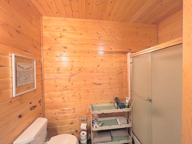 bathroom with a shower with door, toilet, wood ceiling, and wood walls