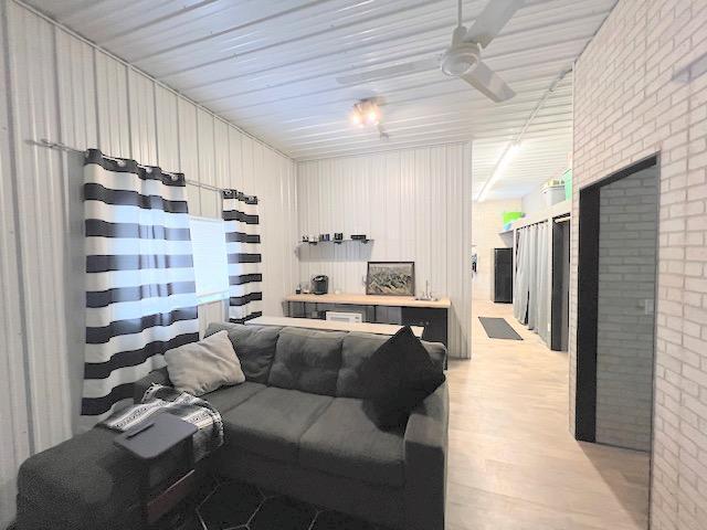 living room with light hardwood / wood-style floors, ceiling fan, and brick wall