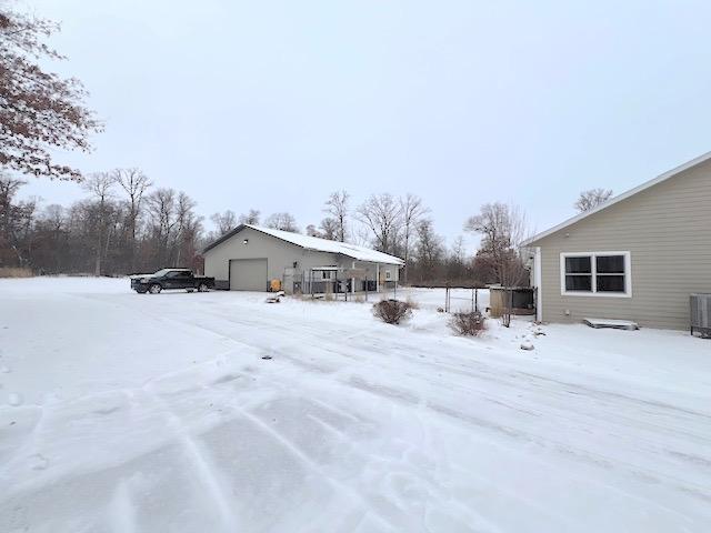 yard layered in snow featuring a garage, central AC unit, and an outdoor structure