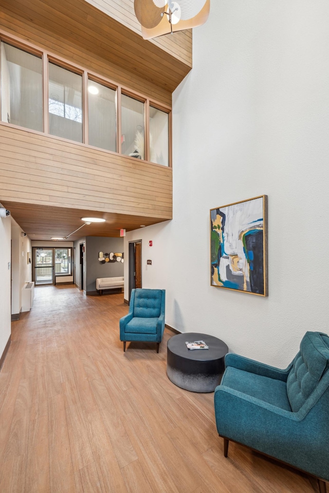 sitting room with hardwood / wood-style flooring, ceiling fan, wooden ceiling, and a towering ceiling