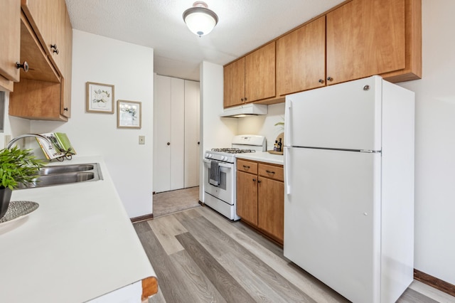 kitchen with a textured ceiling, sink, white appliances, and light hardwood / wood-style flooring