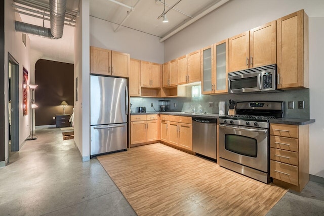 kitchen with appliances with stainless steel finishes, light brown cabinetry, tasteful backsplash, sink, and a high ceiling