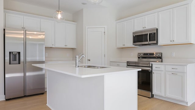 kitchen with appliances with stainless steel finishes, a kitchen island with sink, sink, decorative light fixtures, and light hardwood / wood-style flooring