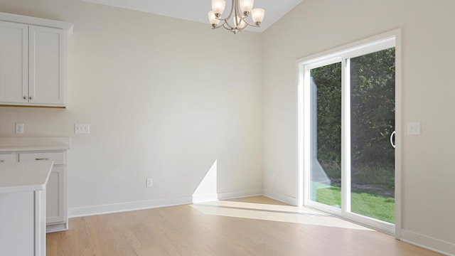 unfurnished dining area with a chandelier, light hardwood / wood-style floors, a wealth of natural light, and vaulted ceiling