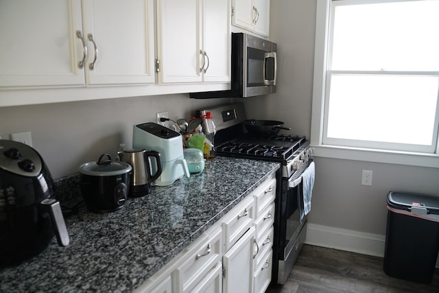 kitchen featuring dark hardwood / wood-style flooring, white cabinets, dark stone counters, and appliances with stainless steel finishes