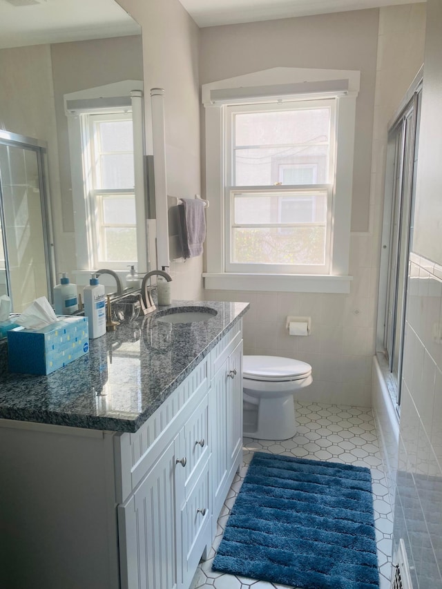 full bathroom featuring vanity, tile patterned floors, bath / shower combo with glass door, toilet, and tile walls