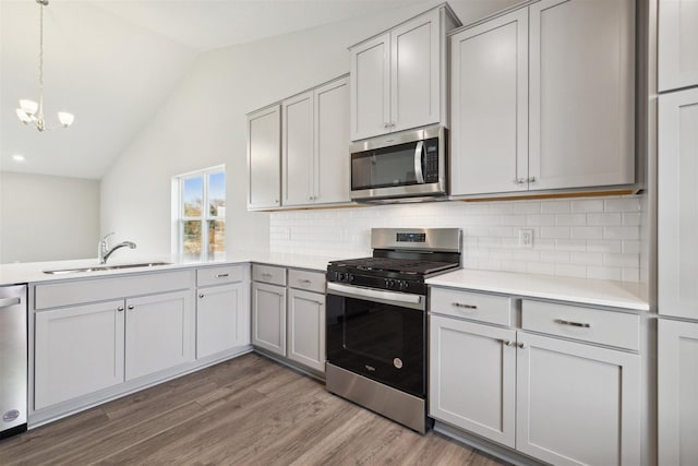 kitchen with lofted ceiling, sink, decorative light fixtures, wood-type flooring, and stainless steel appliances