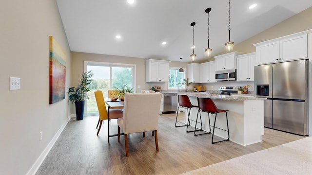 kitchen with pendant lighting, lofted ceiling, appliances with stainless steel finishes, a kitchen island, and white cabinetry