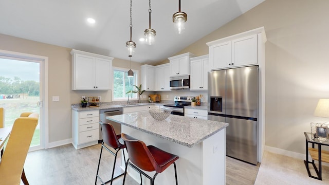 kitchen with hanging light fixtures, stainless steel appliances, a kitchen island, vaulted ceiling, and white cabinets