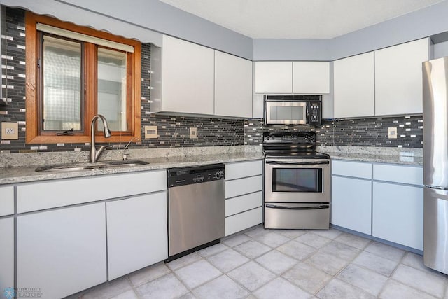 kitchen featuring appliances with stainless steel finishes, white cabinets, a sink, and tasteful backsplash