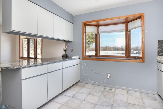 kitchen featuring kitchen peninsula, white cabinetry, plenty of natural light, and dark stone countertops