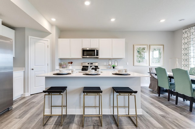 kitchen featuring a kitchen bar, light wood-type flooring, stainless steel appliances, a center island with sink, and white cabinetry