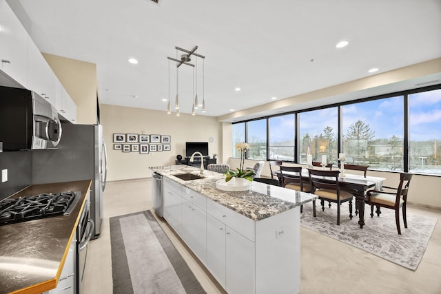 kitchen with sink, a center island with sink, dark stone countertops, white cabinets, and hanging light fixtures