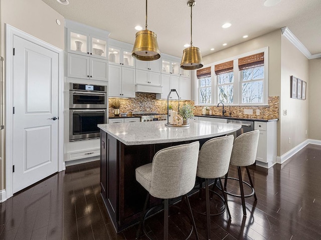 kitchen featuring stainless steel appliances, pendant lighting, white cabinets, light stone counters, and a center island