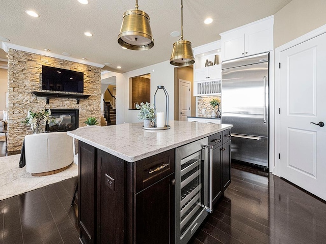 kitchen featuring pendant lighting, beverage cooler, a kitchen island, stainless steel built in fridge, and a stone fireplace