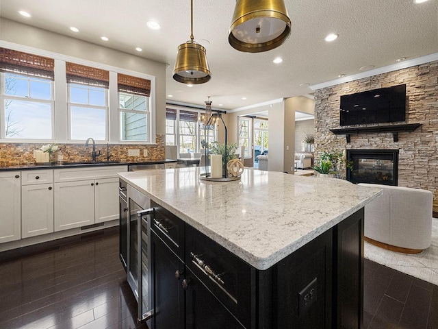 kitchen with decorative light fixtures, a fireplace, a center island, sink, and light stone countertops