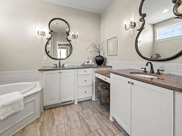 bathroom featuring a textured ceiling, a tub to relax in, and vanity