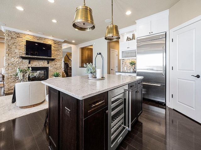 kitchen with beverage cooler, built in fridge, a kitchen island, decorative light fixtures, and white cabinets