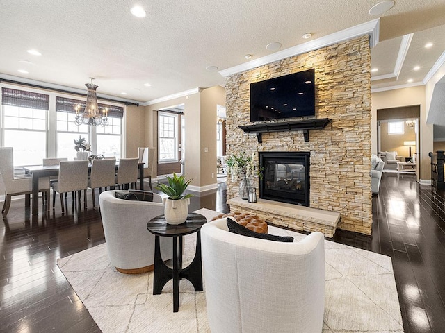 living room featuring a notable chandelier, a textured ceiling, dark hardwood / wood-style floors, a fireplace, and ornamental molding