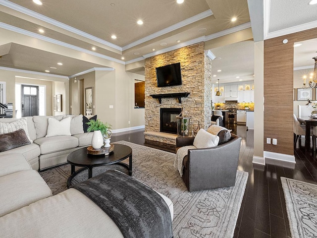 living room featuring dark hardwood / wood-style flooring, an inviting chandelier, a stone fireplace, ornamental molding, and a raised ceiling