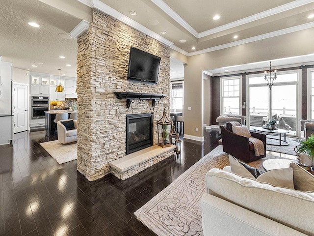 living room with a notable chandelier, dark wood-type flooring, a stone fireplace, and ornamental molding