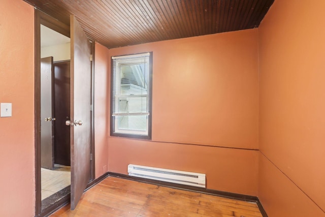 empty room featuring wooden ceiling, light hardwood / wood-style floors, and a baseboard heating unit