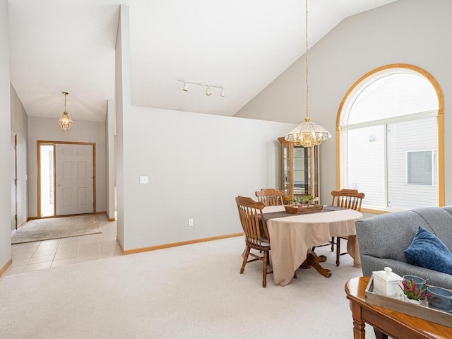 dining space featuring an inviting chandelier, high vaulted ceiling, light colored carpet, and rail lighting