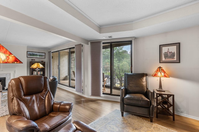 sitting room with a fireplace, wood-type flooring, a tray ceiling, and crown molding