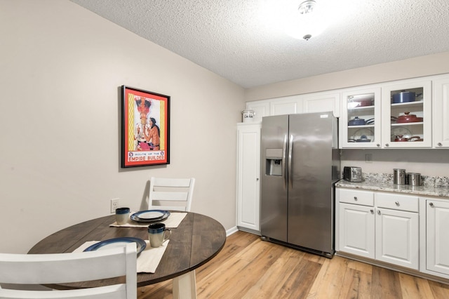 kitchen featuring stainless steel fridge, light wood-type flooring, a textured ceiling, light stone counters, and white cabinetry