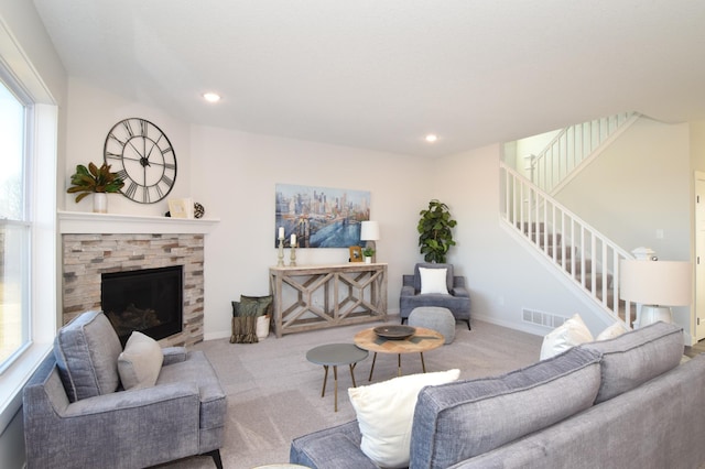 living room featuring a stone fireplace, light carpet, and plenty of natural light