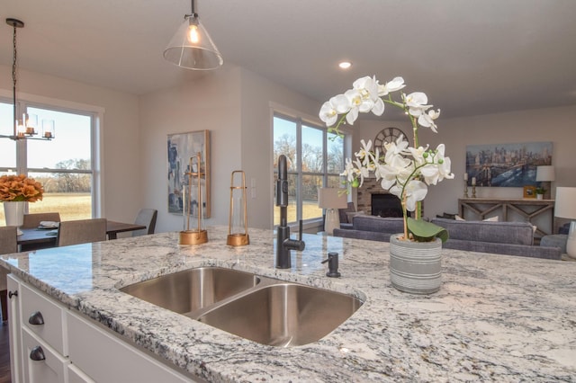 kitchen featuring pendant lighting, sink, light stone countertops, white cabinetry, and a chandelier