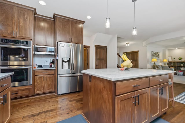 kitchen featuring appliances with stainless steel finishes, light stone counters, dark wood-type flooring, a kitchen island, and hanging light fixtures