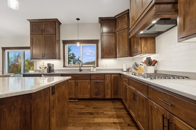 kitchen featuring stainless steel gas cooktop, sink, premium range hood, pendant lighting, and light stone countertops