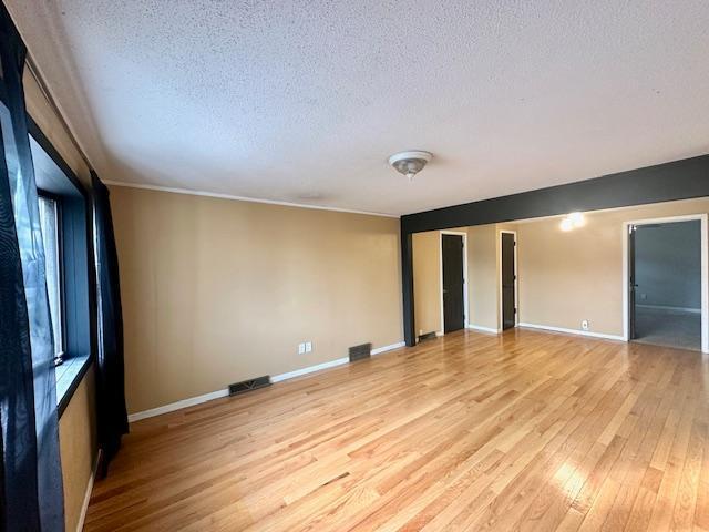 unfurnished room with crown molding, a textured ceiling, and light wood-type flooring