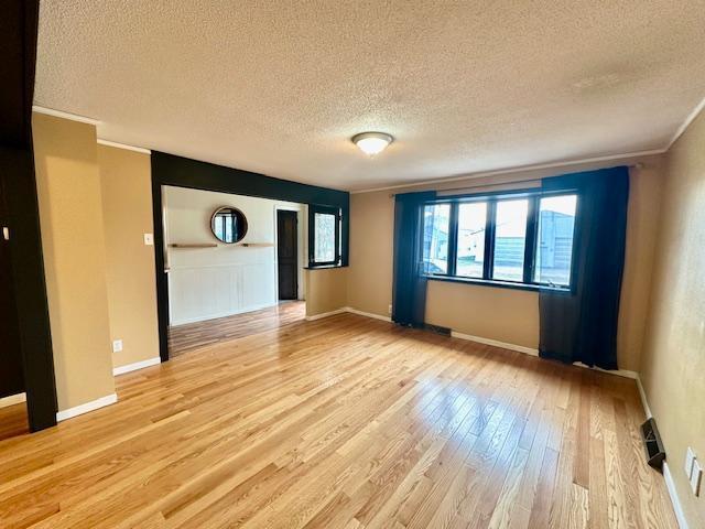 spare room featuring light hardwood / wood-style floors, ornamental molding, and a textured ceiling