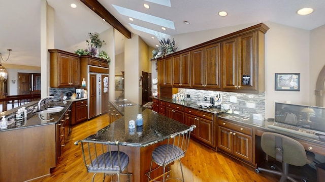 kitchen featuring backsplash, a center island, lofted ceiling with skylight, and dark stone counters