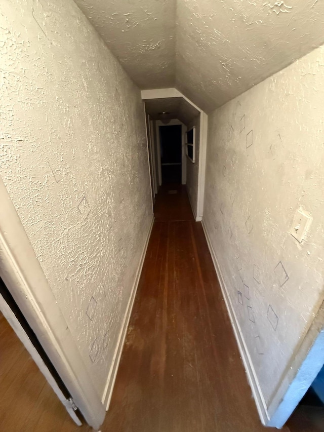 corridor featuring dark hardwood / wood-style flooring, a textured ceiling, and vaulted ceiling