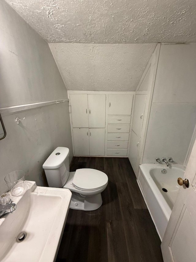 bathroom with a tub, sink, a textured ceiling, lofted ceiling, and hardwood / wood-style flooring