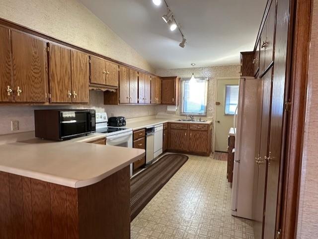 kitchen with lofted ceiling, white appliances, sink, decorative light fixtures, and kitchen peninsula