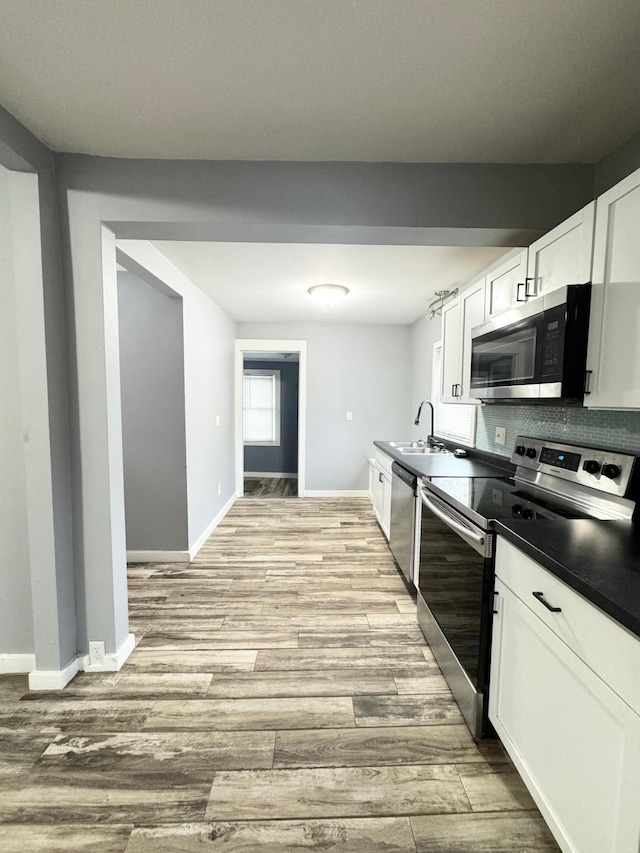 kitchen featuring decorative backsplash, light wood-type flooring, stainless steel appliances, sink, and white cabinets